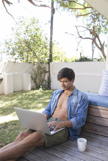 Mann sitzt auf einer Terrasse im Garten und benutzt einen Laptop - WESTF23170