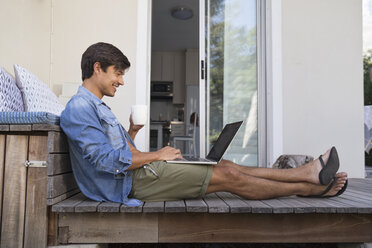 Mann sitzt auf einer Terrasse und benutzt einen Laptop - WESTF23171