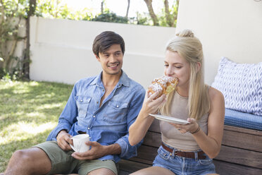 Lächelnder Mann sitzt auf der Terrasse und beobachtet seine Freundin beim Essen - WESTF23177