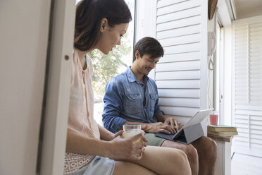 Young couple sitting on windowsill with drink and tablet - WESTF23194