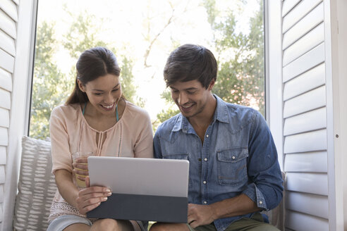 Lächelndes junges Paar sitzt auf der Fensterbank und teilt sich ein Tablet - WESTF23195