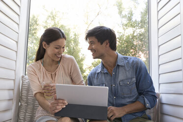 Smiling young couple sitting on windowsill sharing tablet - WESTF23196