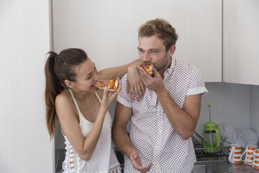 Glückliches junges Paar isst Pizza in der Küche - WESTF23260