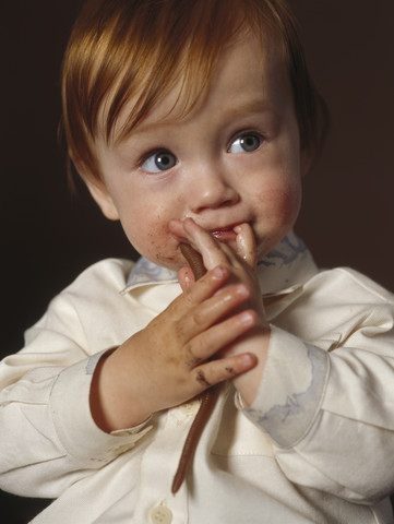 Porträt eines rothaarigen kleinen Jungen mit Spielzeugwurm und Finger im Mund, lizenzfreies Stockfoto