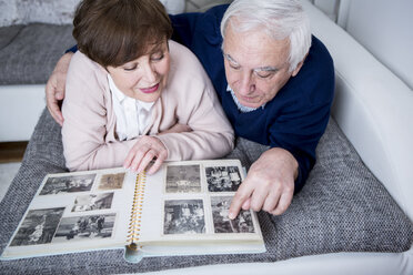 Senior couple lying on couch, looking at photo album - WESTF23272