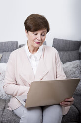 Ältere Frau sitzt auf der Couch und benutzt einen Laptop - WESTF23273