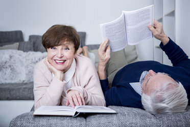 Senior couple lying on couch, reading books - WESTF23275