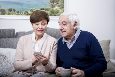 Senior couple lying on couch using smartphone - WESTF23287