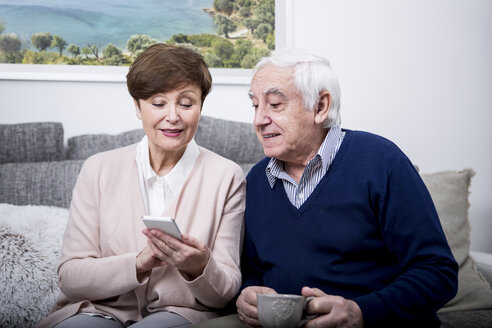 Älteres Ehepaar liegt auf der Couch und benutzt ein Smartphone - WESTF23287