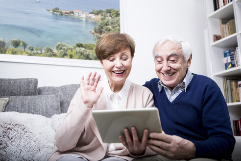Ein älteres Ehepaar sitzt auf der Couch und führt einen Videoanruf auf seinem digitalen Tablet durch - WESTF23290