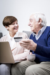 Senior couple lying on couch doing online shopping with credit card - WESTF23292