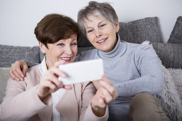 Zwei ältere Frauen sitzen auf der Couch und machen Selfies - WESTF23301