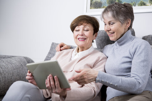 Zwei ältere Frauen sitzen auf einer Couch und schauen auf ein digitales Tablet - WESTF23303