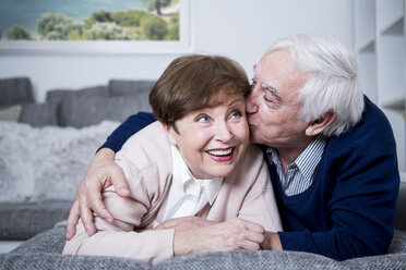 Senior couple lying on couch, hugging and kissing - WESTF23306