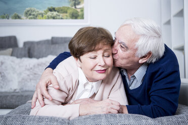 Senior couple lying on couch, hugging and kissing - WESTF23307
