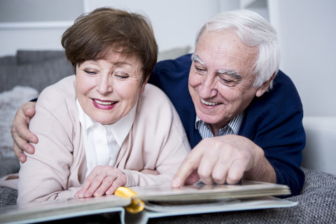 Älteres Paar liegt auf der Couch und betrachtet ein Fotoalbum, lizenzfreies Stockfoto
