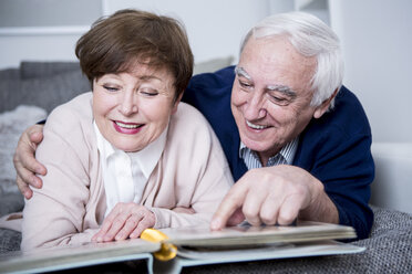 Senior couple lying on couch, looking at photo album - WESTF23309