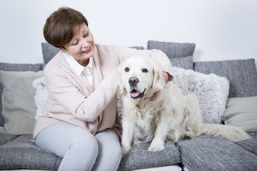 Senior woman sitting on couch with her dog - WESTF23313