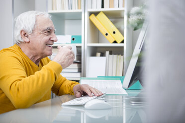 Älterer Mann arbeitet am Computer mit einer Tasse Kaffee - WESTF23324