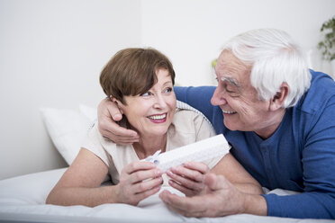 Älteres Paar im Bett liegend, Mann überreicht der Frau ein Geschenk - WESTF23339