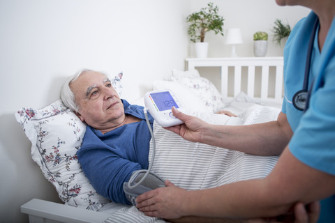 Gynäkologin misst den Blutdruck eines im Bett liegenden Patienten, lizenzfreies Stockfoto