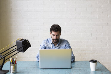 Ernster Mann sitzt am Schreibtisch und arbeitet mit seinem Laptop - ABZF02055