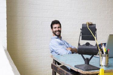 Portrait of smiling man relaxing at desk in his loft - ABZF02060