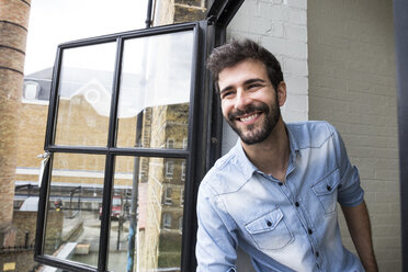 Portrait of smiling young man leaning out of the window - ABZF02072