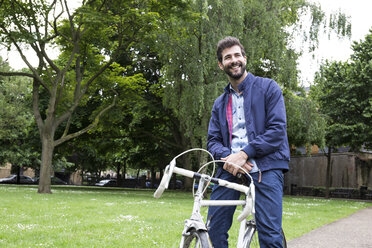 Lächelnder junger Mann mit Fahrrad in einem Park - ABZF02075