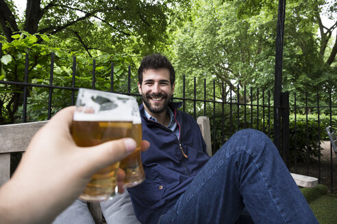 Porträt eines lächelnden jungen Mannes, der mit einem Glas Bier im Garten anstößt - ABZF02076