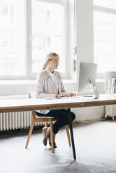 Geschäftsfrau sitzt am Schreibtisch und arbeitet mit dem Computer - JOSF01060