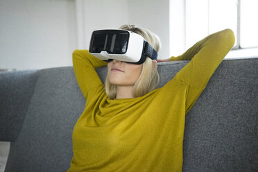 Woman sitting on couch wearing virtual reality glasses - JOSF01070