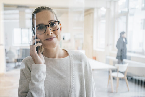 Porträt einer lächelnden Geschäftsfrau am Telefon im Büro - JOSF01074