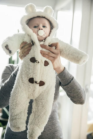 Mutter hält Baby im Eisbärenkostüm hoch, lizenzfreies Stockfoto