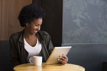 Lachende junge Frau, die in einem Café sitzt und auf ein Tablet schaut - ABZF02083