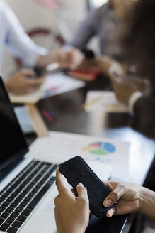 Geschäftsfrau benutzt Mobiltelefon während einer Besprechung im Büro - GIOF02655