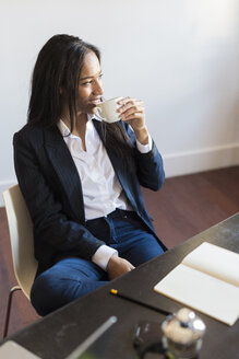 Lächelnde Geschäftsfrau beim Kaffeetrinken während einer Sitzung im Büro - GIOF02665
