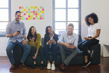 Portrait of happy colleagues sitting on couch with cell phones - GIOF02699