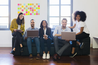 Portrait of happy colleagues sitting on couch with laptops - GIOF02701