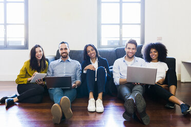 Portrait of happy colleagues sitting on couch with laptops - GIOF02703