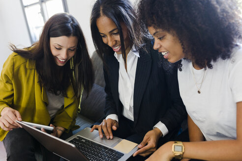 Drei lächelnde Geschäftsfrauen teilen sich einen Laptop im Büro - GIOF02705