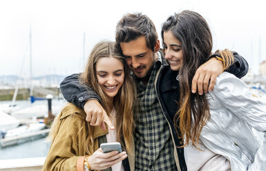 Drei Freunde schauen auf ihr Handy im Yachthafen - MGOF03415