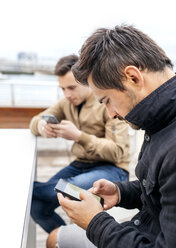 Zwei Männer senden Nachrichten mit ihren Smartphones - MGOF03418