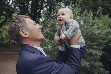 Happy mature businessman holding up baby boy outdoors - MFF03613