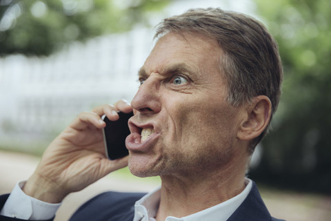 Porträt eines wütenden reifen Geschäftsmannes, der im Freien telefoniert, lizenzfreies Stockfoto