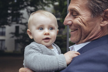 Happy mature businessman holding baby boy outdoors - MFF03619