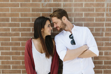 Happy couple standing in front of brick wall, kissing - GIOF02712