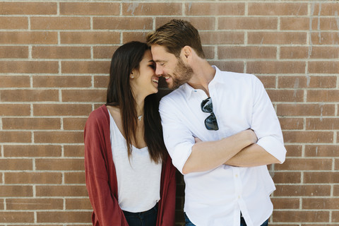Glückliches Paar steht vor einer Backsteinmauer und küsst sich, lizenzfreies Stockfoto