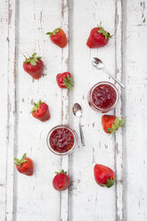 Two glasses of homemade strawberry jam, tea spoons and strawberries on white wood - LVF06151