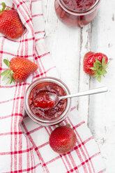 Glass of homemade strawberry jam, kitchen towel and strawberries on white wood - LVF06155